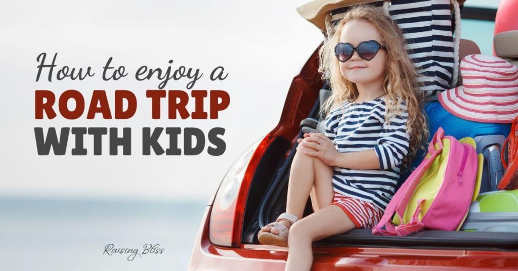 Little girl sitting in the trunk of a car with suitcases. How to enjoy a road trip with kids by raising bliss