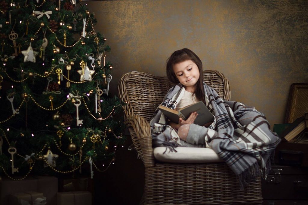 Young Girl reading a book by the christmas tree